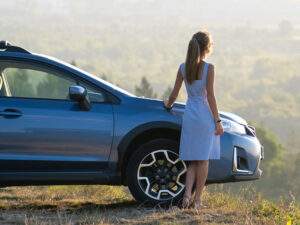 Young woman standing by a car overlooking scenery in Saginaw, with auto insurance coverage